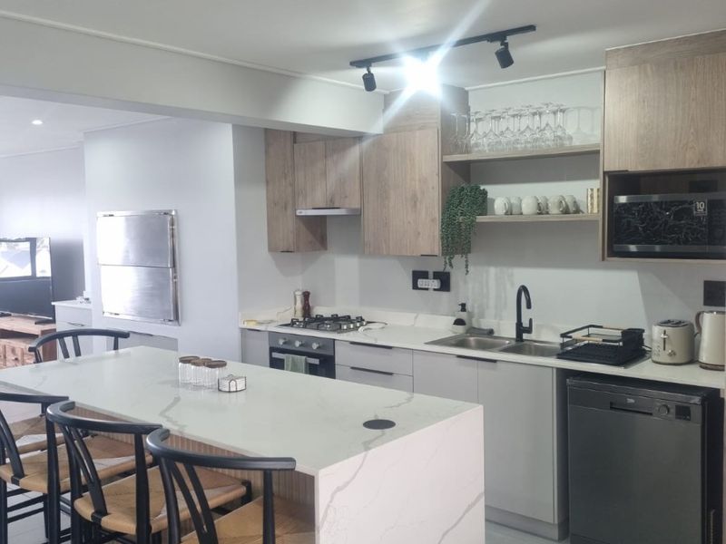 Modern open-plan kitchen featuring a stone-topped island, integrated appliances, sleek cabinetry, and contemporary track lighting, creating a functional and stylish culinary space.