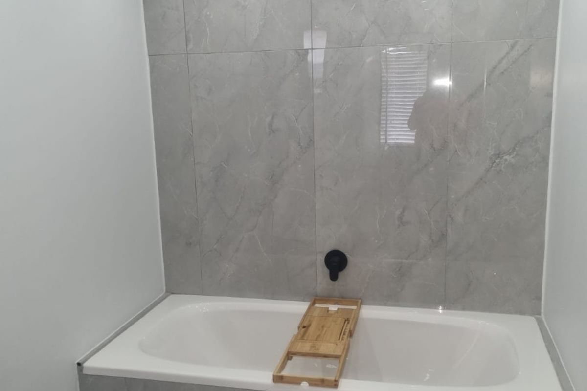 Modern bathroom featuring a built-in bathtub with contemporary grey marble-look tiling and sleek black fixtures.