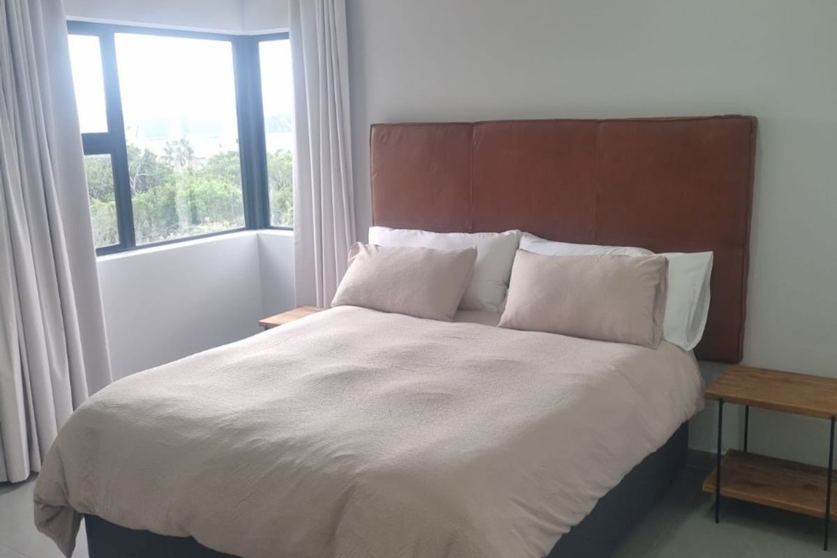 A modern, well-maintained bedroom featuring neutral tiled flooring, recessed downlighting, and a large corner window providing natural light.