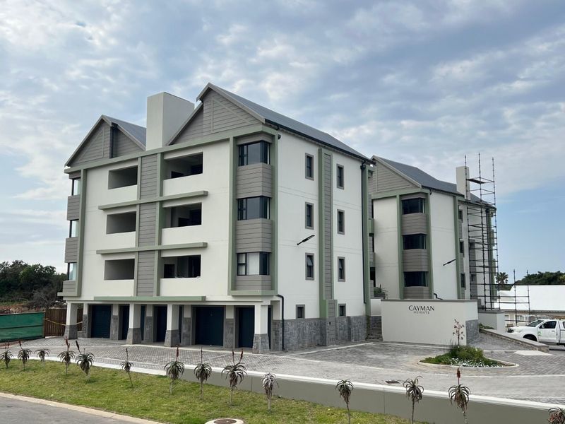Front elevation of the Cayman Heights apartment complex, featuring modern architectural design, paved driveway, and balconies, currently undergoing final construction phases.