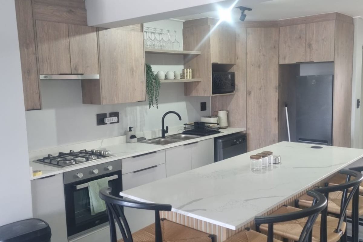Modern kitchen featuring wood-tone cabinetry, stone countertops, a central island with breakfast bar seating, and integrated appliances.