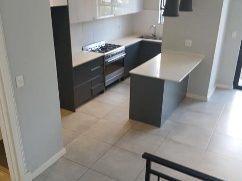 Modern kitchen featuring sleek two-tone cabinetry, stone countertops, a gas stove, and a functional island, finished with neutral floor tiles.