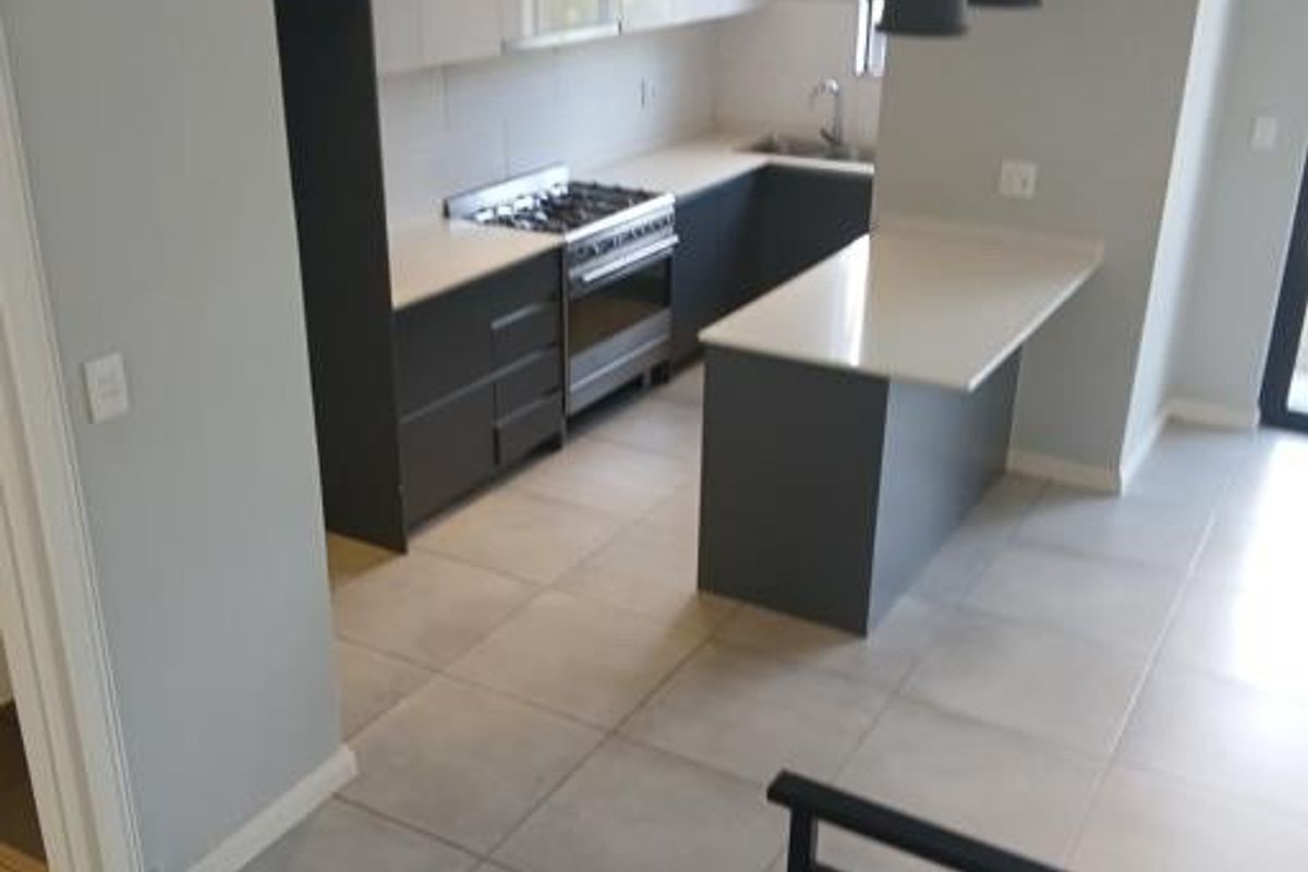 Modern kitchen featuring sleek two-tone cabinetry, stone countertops, a gas stove, and a functional island, finished with neutral floor tiles.