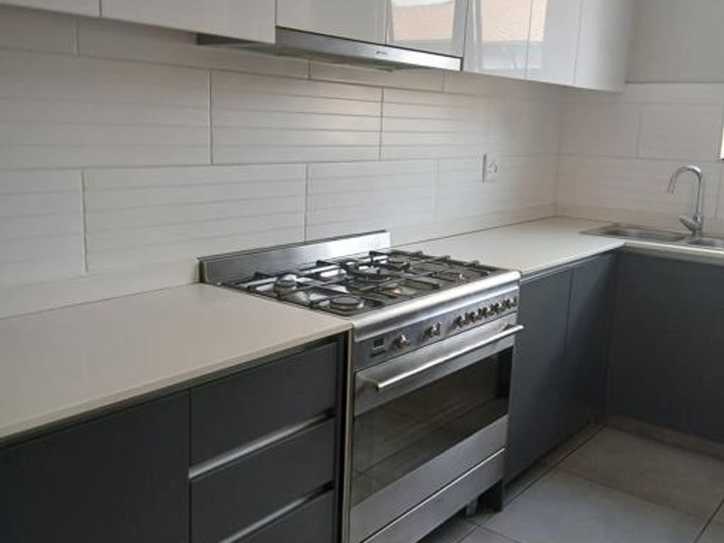 Modern kitchen featuring sleek grey and white cabinetry, stone countertops, a gas hob with extractor fan, and a stainless steel sink.