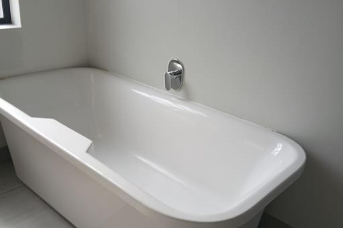 A clean, modern bathroom featuring a white freestanding bathtub, chrome mixer tap, and neutral floor tiling.