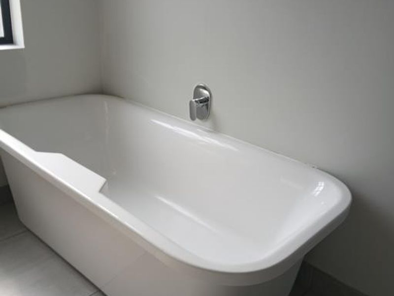 A clean, modern bathroom featuring a white freestanding bathtub, chrome mixer tap, and neutral floor tiling.