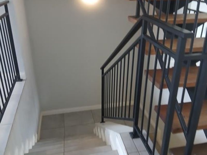 A modern staircase featuring wooden treads, black metal balustrades, and tiled flooring, illuminated by a contemporary wall-mounted light fixture.
