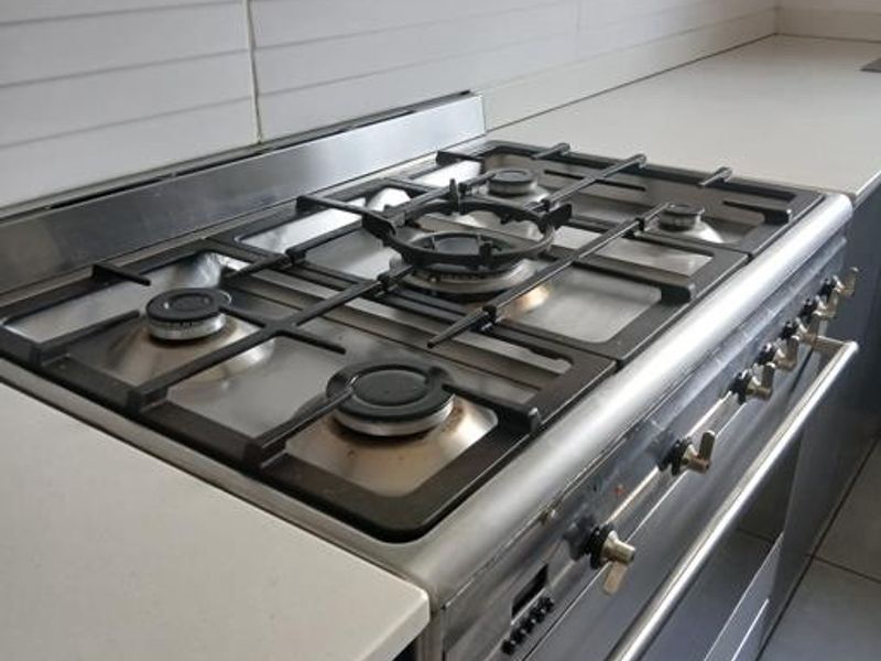 A close-up view of a stainless steel gas hob and built-in oven set into a modern kitchen countertop with a tiled backsplash.
