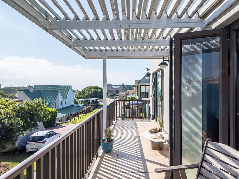 A spacious balcony featuring a modern louvred pergola, tiled flooring, and metal balustrades, offering an elevated outdoor living space with neighbourhood views.