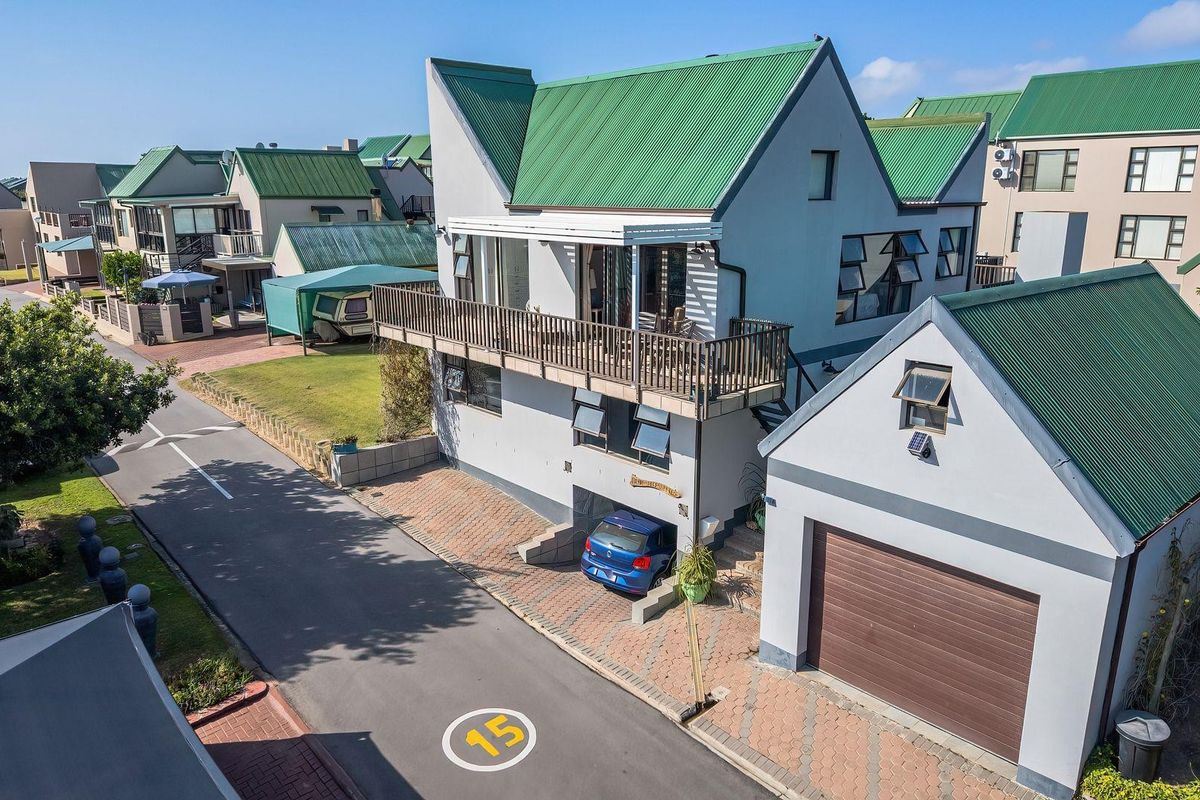 Aerial view of a multi-level residential property featuring a green metal roof, a balcony, a paved driveway, and a detached garage.