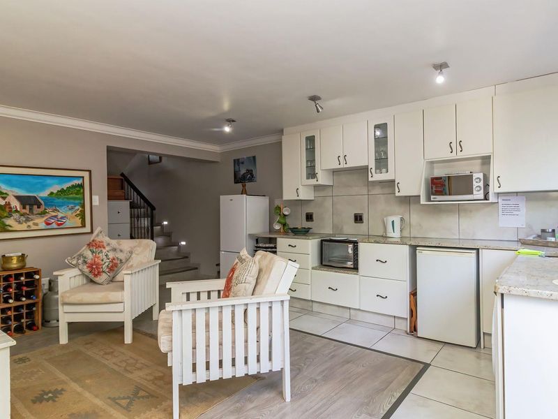 Open-plan living area featuring a functional kitchen with built-in cabinetry, stone countertops, and tiled flooring, seamlessly connected to the staircase and living space.