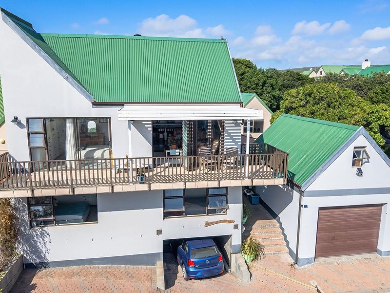 Front elevation of a multi-level house featuring a green corrugated metal roof, a spacious balcony, an integrated garage, and paved driveway parking.