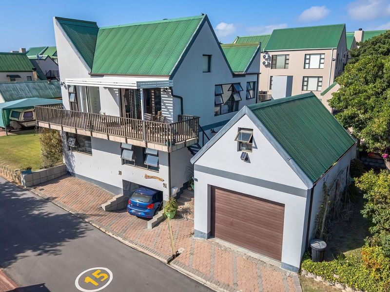 Aerial view of a multi-level residential property featuring a green metal roof, a balcony, and a detached garage with a paved driveway.