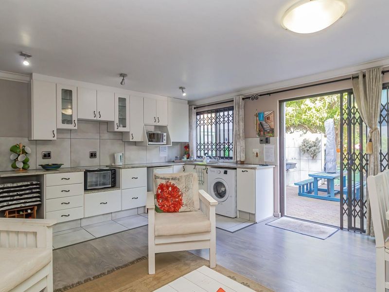 Open-plan kitchen and living area featuring white cabinetry, integrated appliances, and direct access to a paved outdoor patio through a sliding security door.