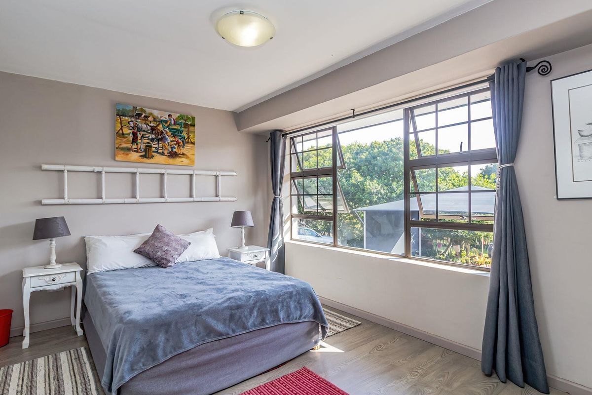 A bright bedroom featuring large windows that provide natural light and views, complemented by neutral wall tones and durable laminate flooring.