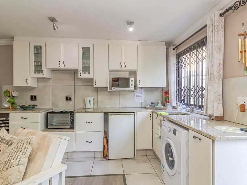 A functional kitchen featuring white cabinetry, granite countertops, tiled backsplash, and integrated appliance spaces with a window security gate.