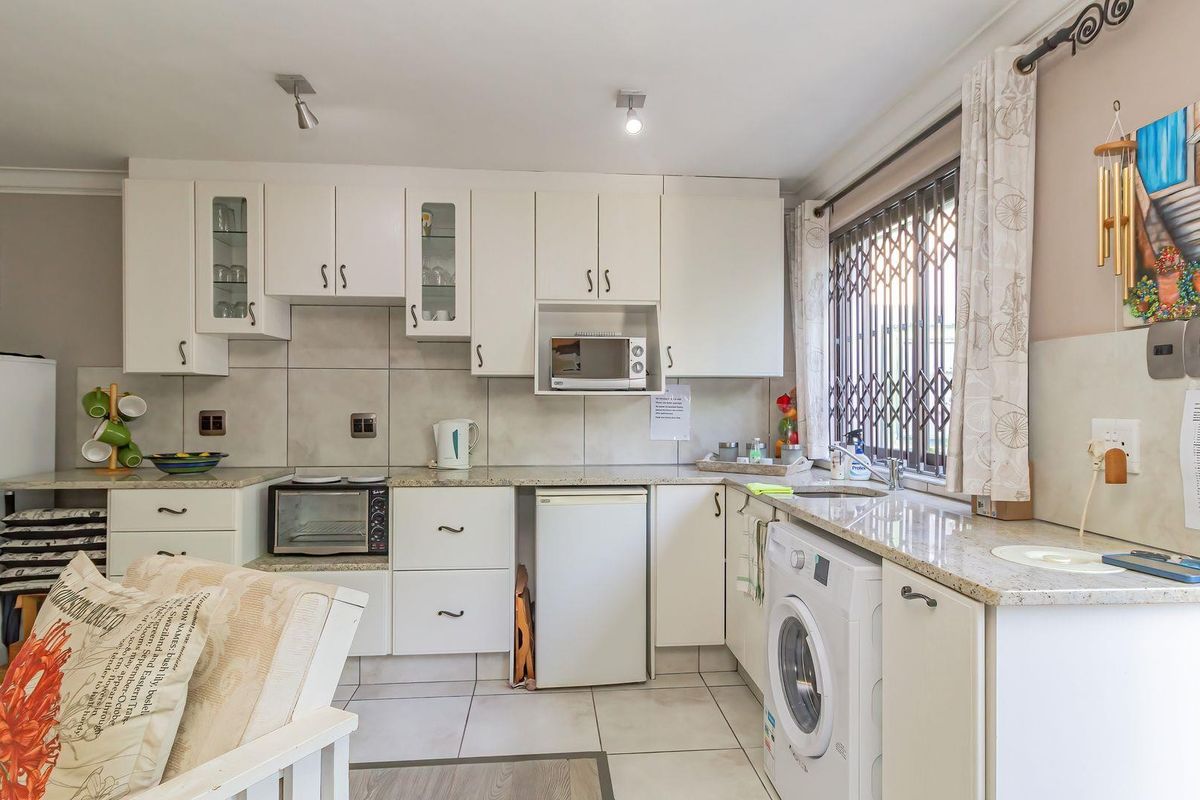 A functional kitchen featuring white cabinetry, granite countertops, tiled backsplash, and integrated appliance spaces with a window security gate.