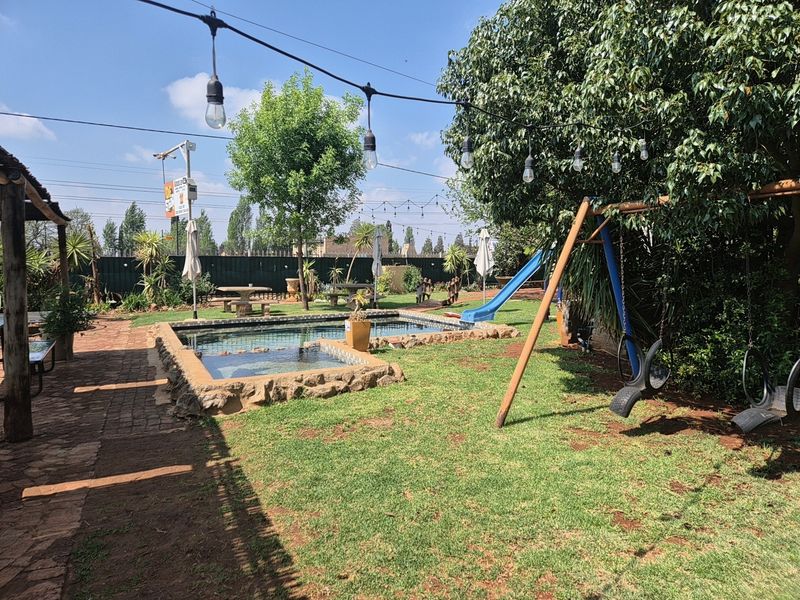 Outdoor pool area featuring a stone-edged swimming pool, paved walkway, and overhead string lighting within a landscaped garden setting.