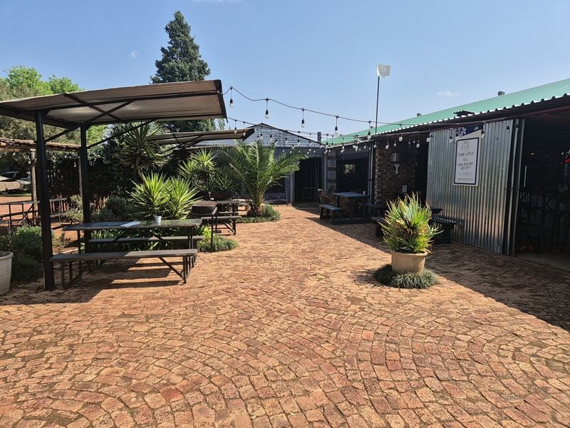 An outdoor patio area featuring brick paving, corrugated metal roofing, and overhead string lighting, suitable for industrial or commercial use.