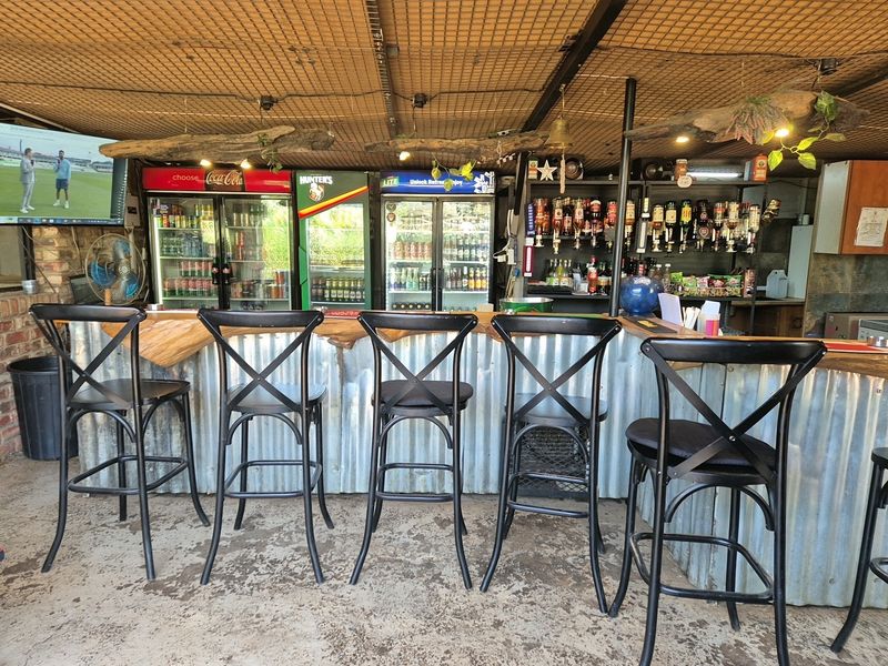 A rustic industrial-style bar area featuring a corrugated metal counter, exposed mesh ceiling, and integrated beverage refrigeration units.