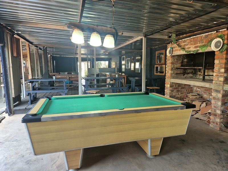 Covered outdoor entertainment area featuring a built-in brick braai, corrugated metal roofing, and concrete flooring, suitable for social gatherings.