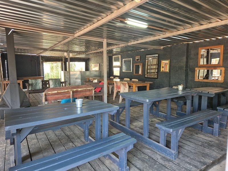 Covered outdoor patio area featuring timber decking, a corrugated metal roof, and a built-in fireplace, suitable for industrial-style entertainment or dining.