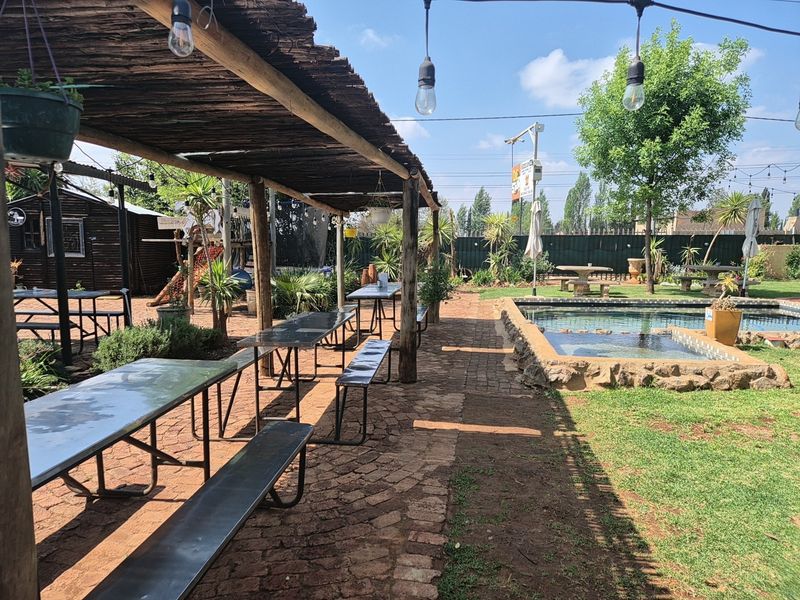 Outdoor entertainment area featuring a thatched pergola, paved walkway, and a swimming pool with stone coping in a landscaped garden setting.