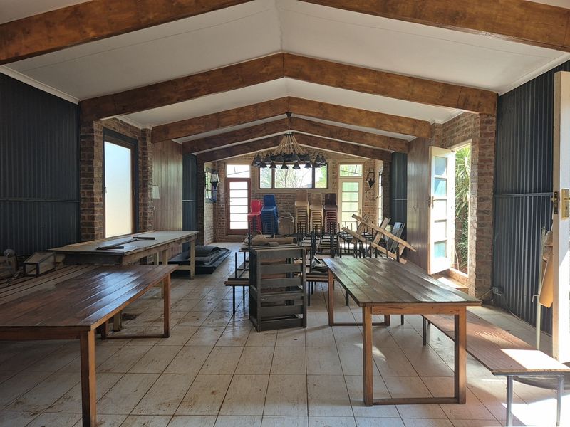 Spacious open-plan industrial area featuring exposed timber roof trusses, brick walls, corrugated metal accents, and multiple access points with tiled flooring.