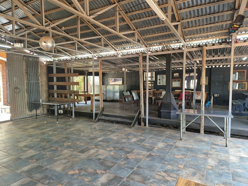 Spacious covered outdoor entertainment area featuring a raised timber deck, tiled flooring, exposed steel roof structure, and a central freestanding fireplace.