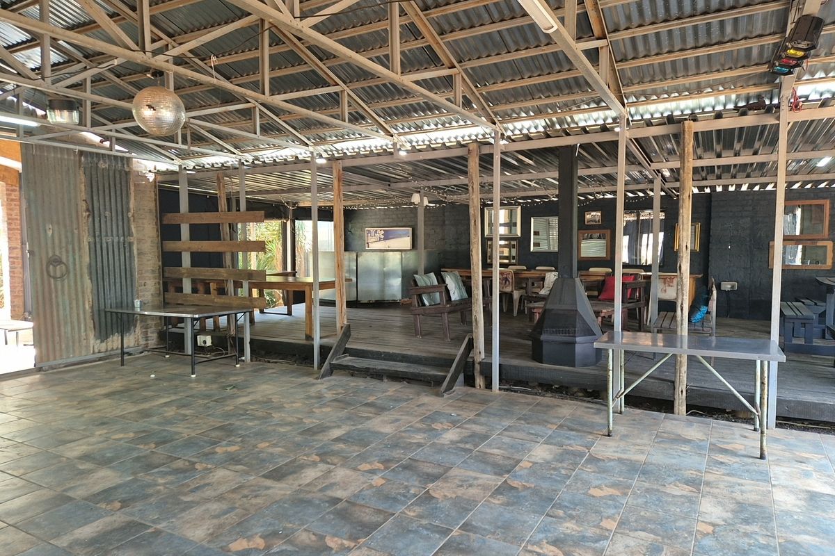 Spacious covered outdoor entertainment area featuring a raised timber deck, tiled flooring, exposed steel roof structure, and a central freestanding fireplace.