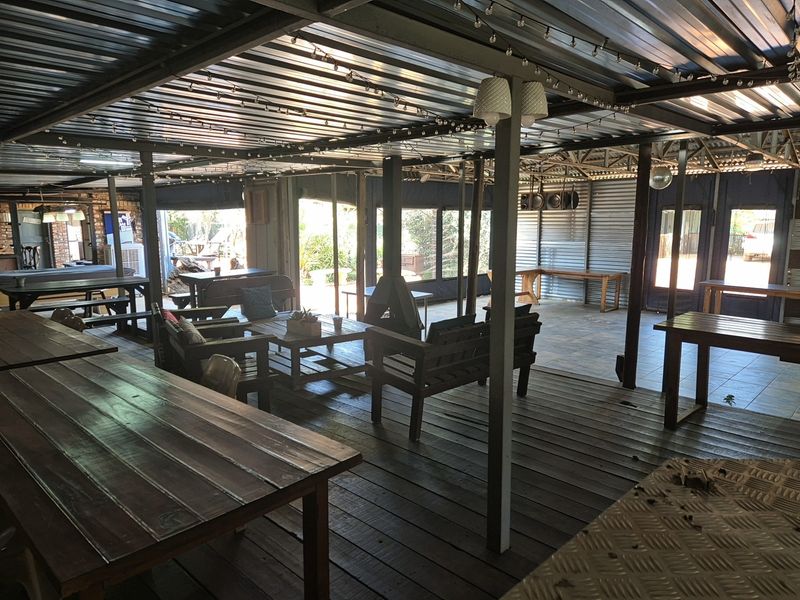 Spacious covered outdoor entertainment area featuring timber decking, tiled sections, a central fireplace, and corrugated metal roofing, ideal for industrial-style gatherings.