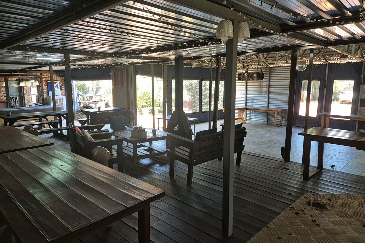 Spacious covered outdoor entertainment area featuring timber decking, tiled sections, a central fireplace, and corrugated metal roofing, ideal for industrial-style gatherings.