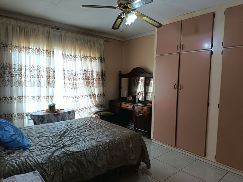 A bedroom featuring built-in cupboards, tiled flooring, and a ceiling fan, offering a functional space with potential for modern updates.