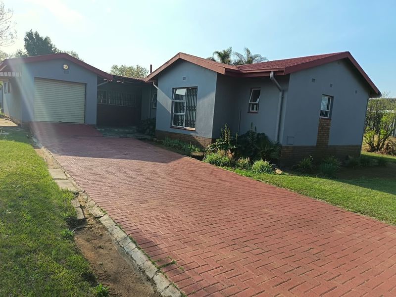 Front view of a single-story house featuring a paved driveway, attached single garage, and grey exterior walls with brick detailing.
