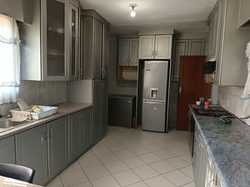 A functional kitchen featuring extensive built-in cabinetry, tiled flooring, and a tiled backsplash, offering a practical layout with ample storage space.