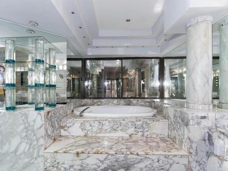 Spacious bathroom featuring a raised built-in marble bathtub, extensive marble wall finishes, mirrored accents, and recessed ceiling lighting.