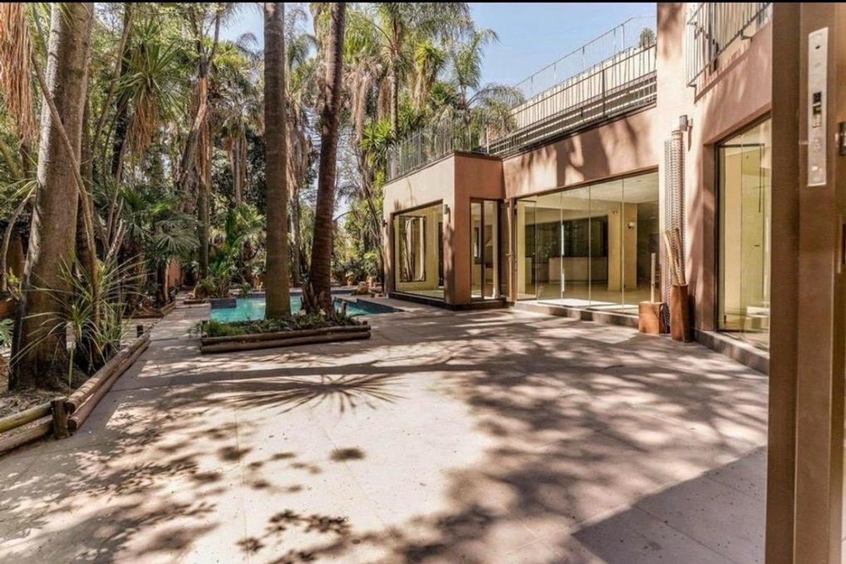 A spacious rear patio area featuring a swimming pool, mature trees, and large glass sliding doors leading into the home.