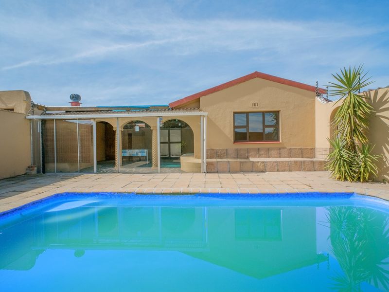 Rear exterior view featuring a swimming pool, paved patio area, and a covered veranda attached to the main house structure.