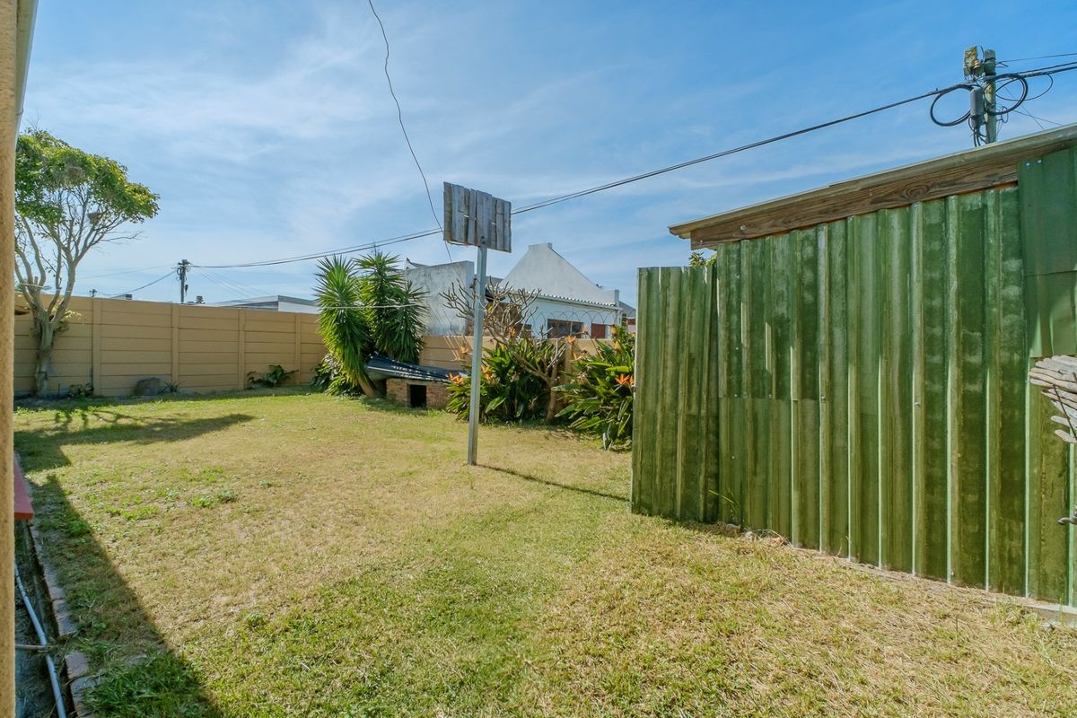 A rear garden area featuring a lawn, a corrugated metal shed, a brick braai, and perimeter precast concrete walling.