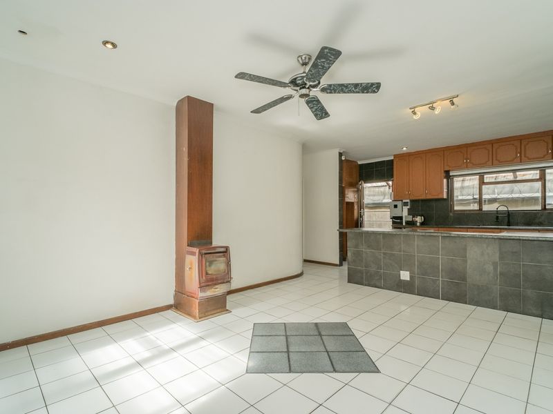 Open-plan living and kitchen area featuring tiled flooring, a central wood-burning fireplace, ceiling fan, and functional kitchen cabinetry with a breakfast counter.