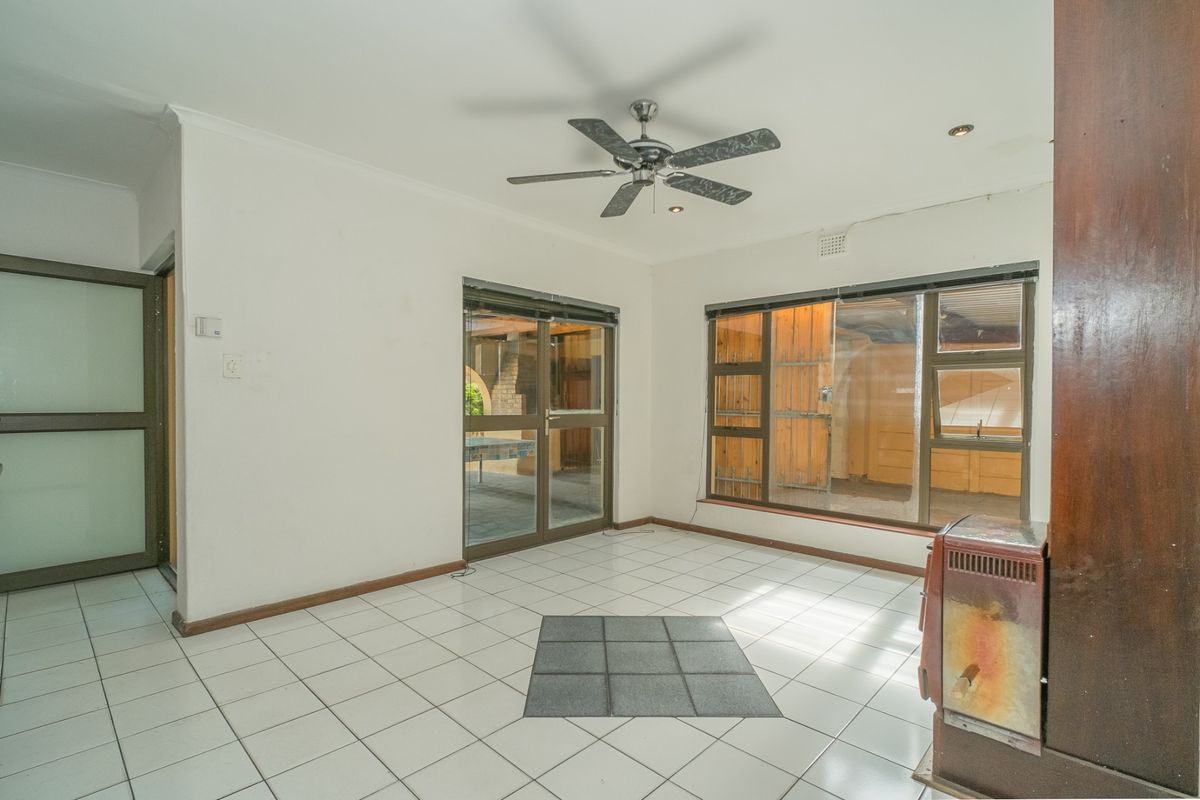 An empty living room featuring tiled flooring, a ceiling fan, and large aluminium windows and sliding doors providing access to the outdoor area.