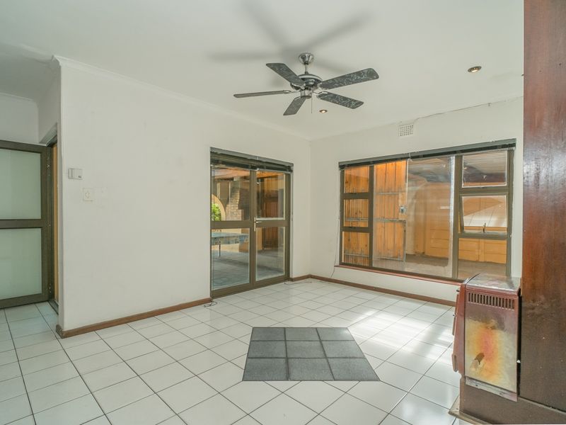 An empty living room featuring tiled flooring, a ceiling fan, and large aluminium windows and sliding doors providing access to the outdoor area.