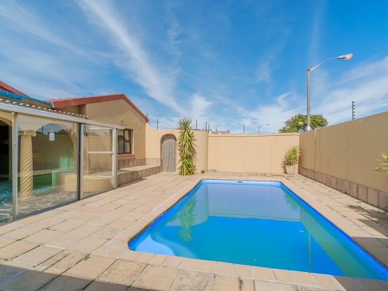 Outdoor pool area featuring a paved deck, boundary wall with electric fencing, and an adjacent enclosed patio space.