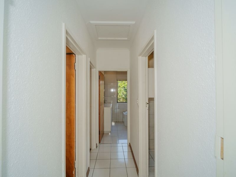 A clean, neutral hallway featuring tiled flooring and access to multiple rooms, providing a functional transition space within the home.