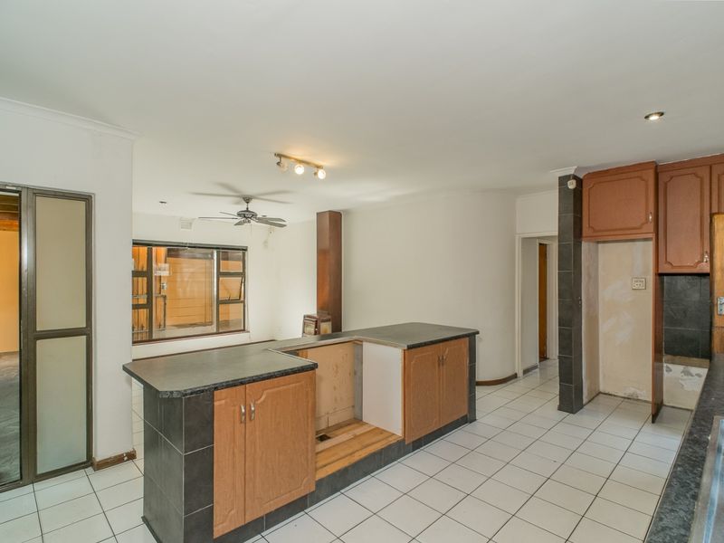 An open-plan kitchen area featuring tiled flooring, a central island with cabinetry, and a double bowl sink, currently requiring cosmetic updates and repairs.