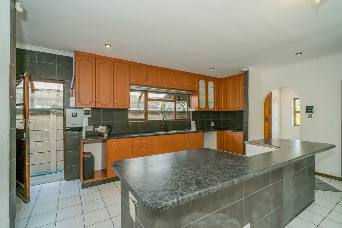 A functional kitchen featuring wooden cabinetry, dark tiled backsplash, and a breakfast bar, offering a practical layout with direct access to an exterior area.
