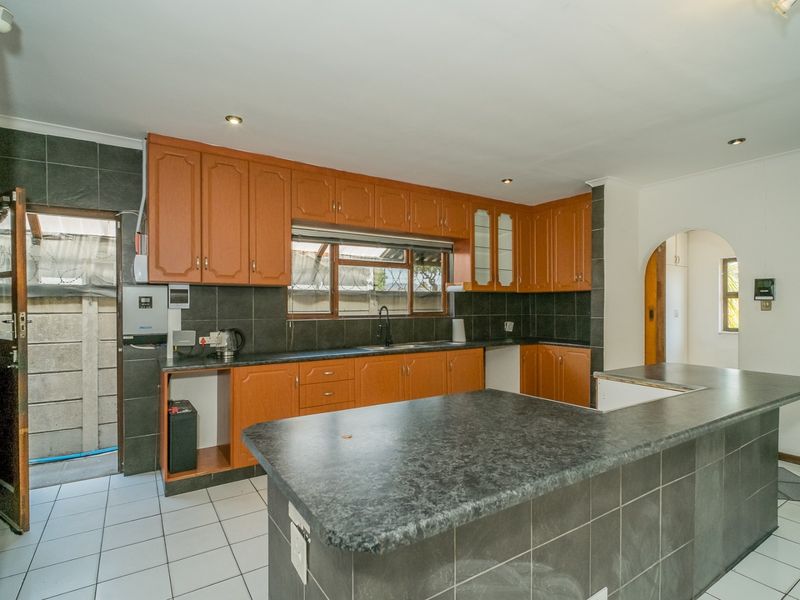 A functional kitchen featuring wooden cabinetry, dark tiled backsplash, and a breakfast bar, offering a practical layout with direct access to an exterior area.