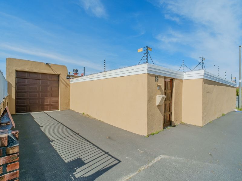 Front exterior view of the property featuring a single garage, secure perimeter wall with electric fencing, and a private pedestrian entrance.