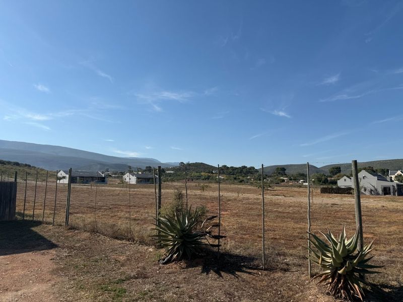 A wide-angle view of a vacant residential plot featuring wire fencing, native vegetation, and surrounding mountain landscape.