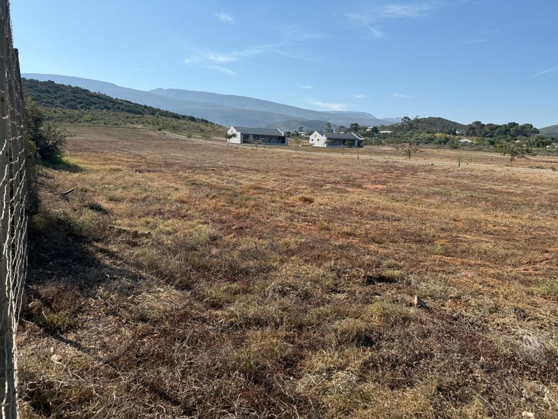 A wide-angle view of a vacant residential plot featuring dry grass, wire mesh perimeter fencing, and scenic mountain views in the background.